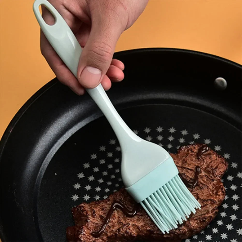 Person using a silicone basting brush to apply oil on a pan with food.