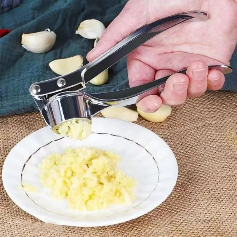 Garlic press being used to crush garlic on a white plate with garlic cloves around.