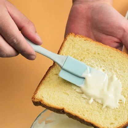 Person spreading butter on a slice of bread using a blue spatula against an orange background