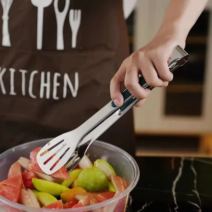Person wearing a brown apron with kitchen utensils holding tongs over a container of fruit salad.