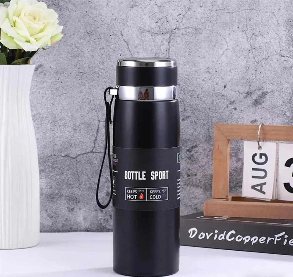 Black insulated bottle with silver lid on a gray surface with decorative items.
