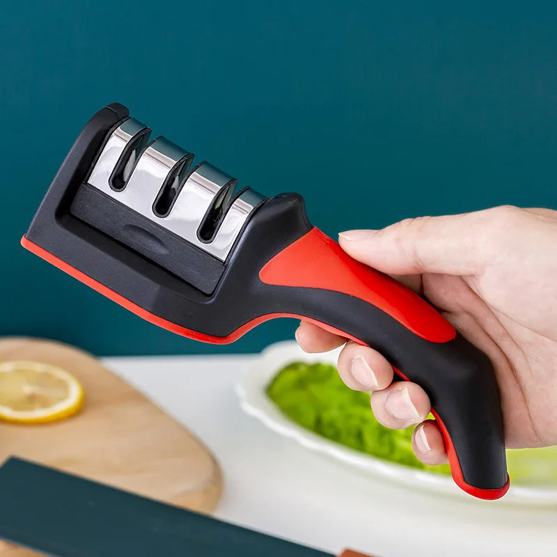 Hand holding a black and red knife sharpener with a kitchen setting in the background