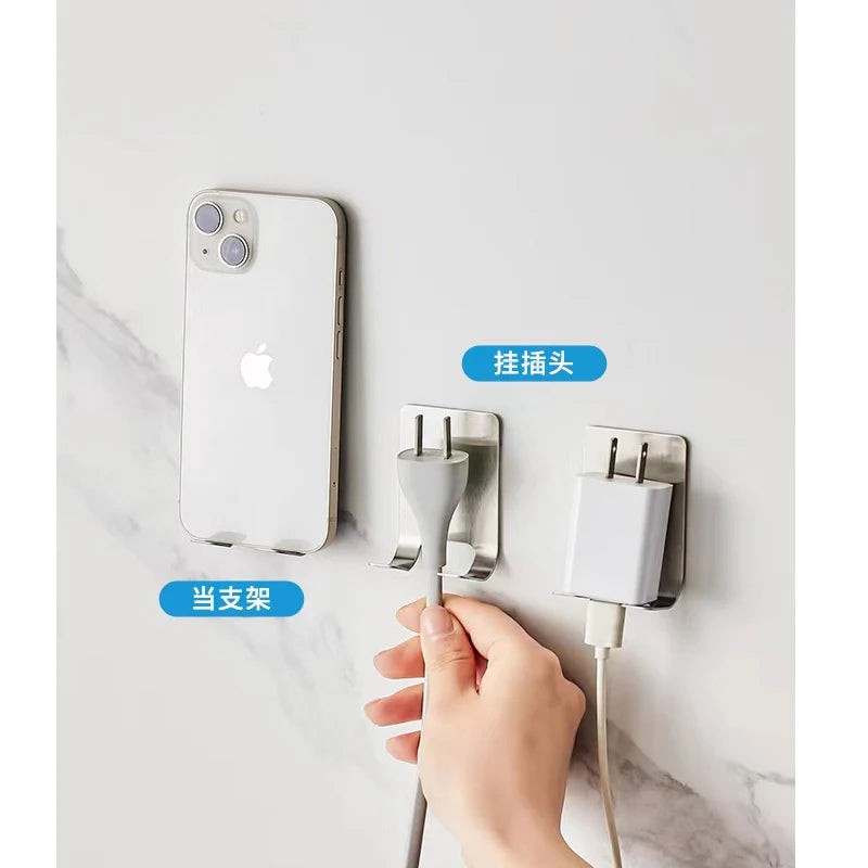 Hand holding a phone and charging cable attached to a wall-mounted holder with smartphone and charger on a white background.